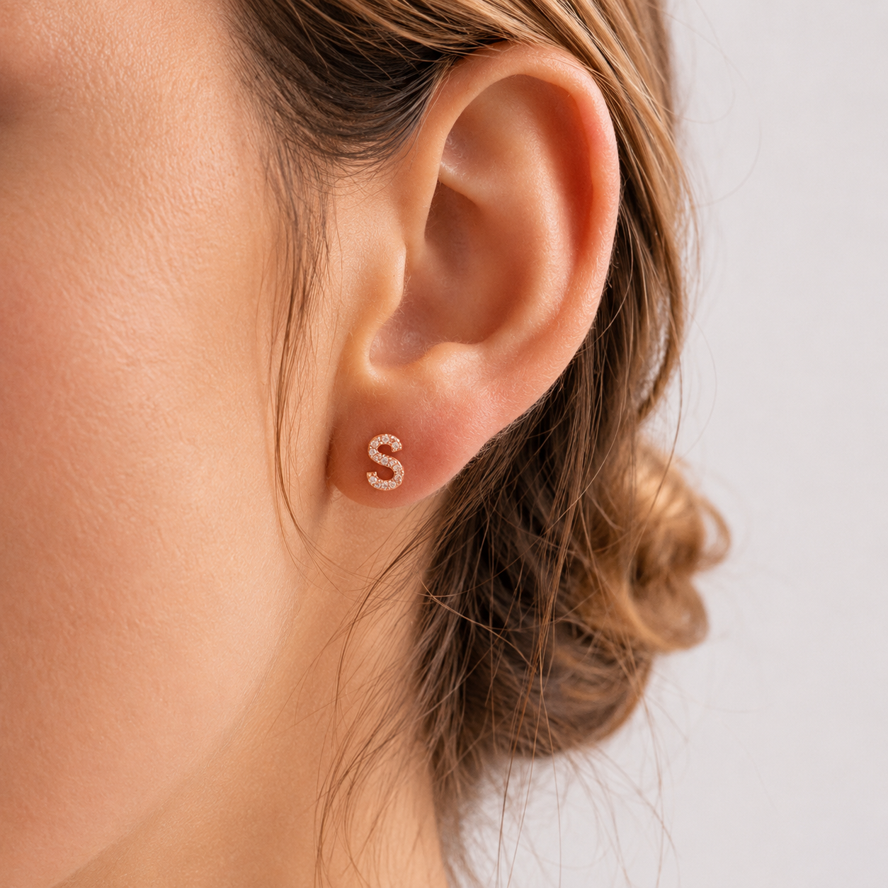 Close-up of an ear wearing a silver 'S' earring on a neutral background